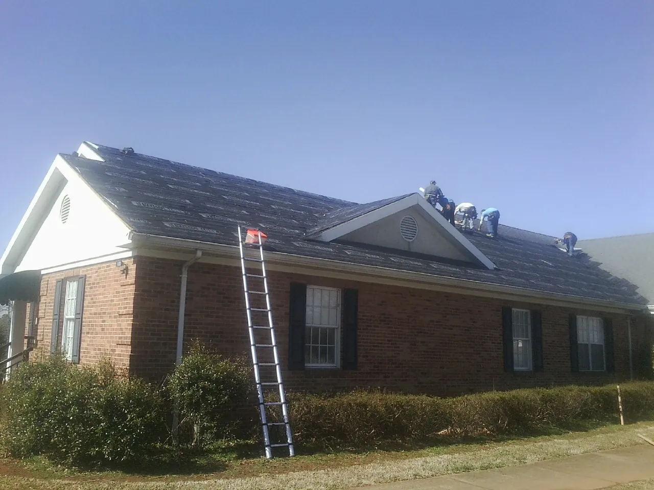 Crew tearing shingles off a brick ranch roof with a ladder set — Emergency Roof Repair work by our crew in Moseley
