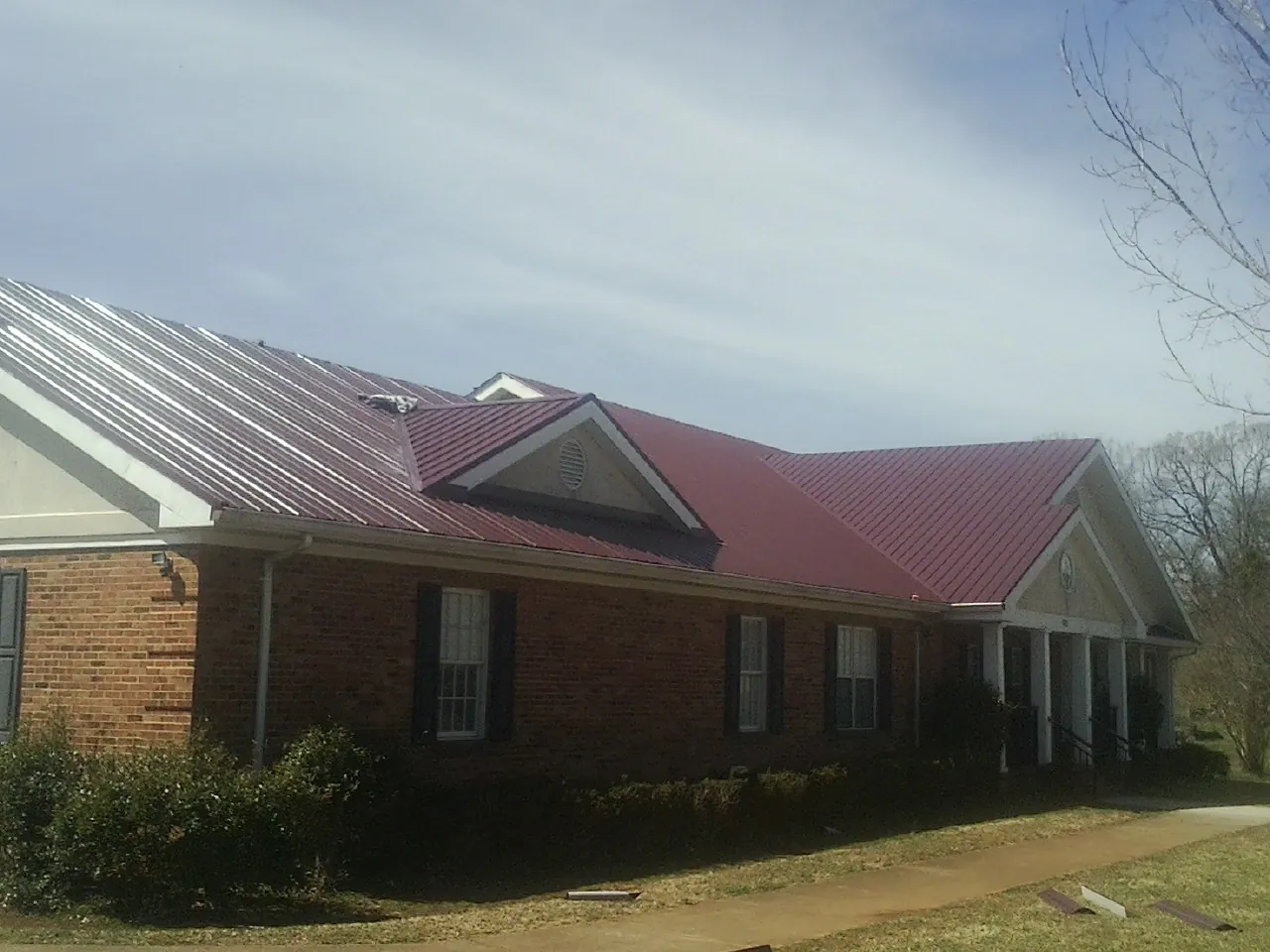 Red metal roof with gabled entries on a long brick building, from a Hail Damage Roof Repair job in Moseley