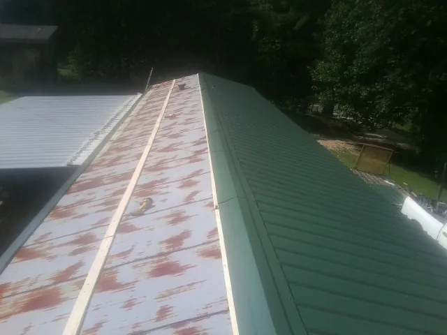 Old rusted panels beside newly installed green metal roofing — Wind Damage Roof Repair by Roofing Brothers in Moseley