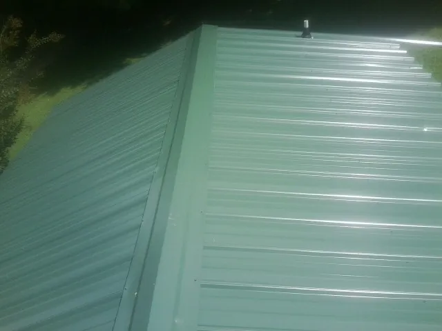 New green metal panels meeting at the ridge of a roof — Flat Roof Repair work by our crew in Moseley