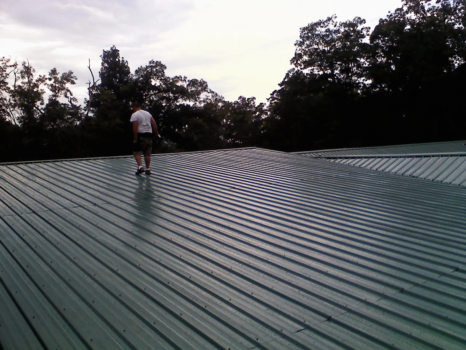 Roofer walking a wide expanse of new green metal roofing in Moseley