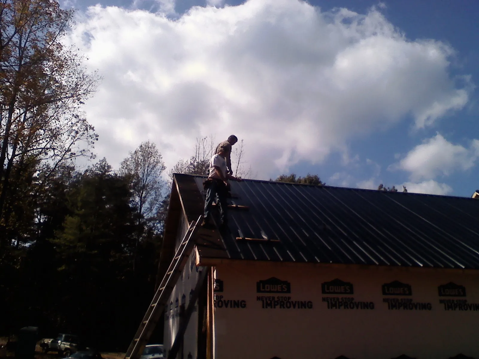 Roofer fastening dark metal panels high against a cloudy sky, from a Roof Inspection job in Moseley
