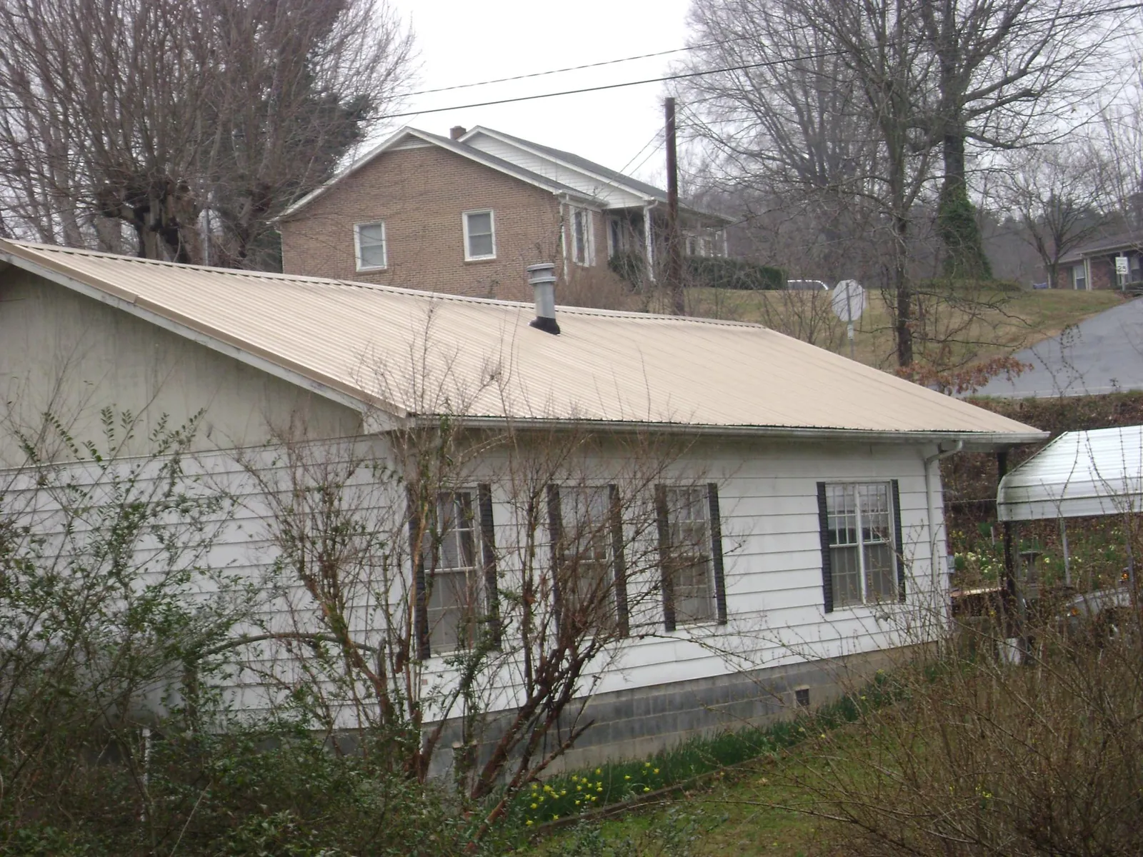 Tan metal roof on a white sided house set into a hillside — Commercial Roofing by Roofing Brothers in Moseley